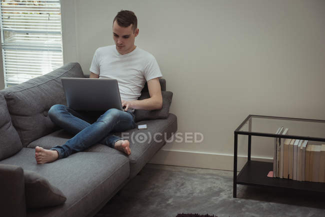 Мужчина использует ноутбук на диване в гостиной дома — стоковое фото