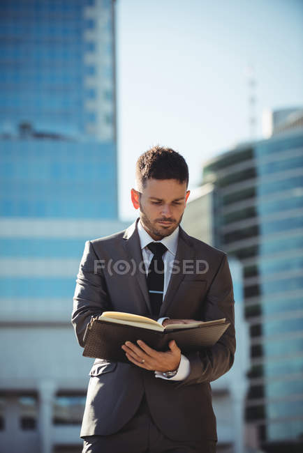 Businessman checking diary book near office building — Stock Photo