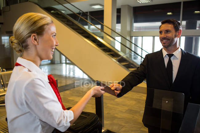 Female staff giving boarding pass to the passenger in the airport terminal — Stock Photo