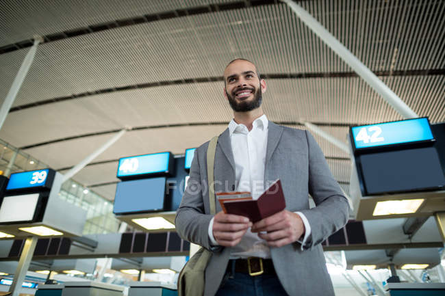 Uomo d'affari sorridente in possesso di carta d'imbarco e passaporto al terminal dell'aeroporto — Foto stock
