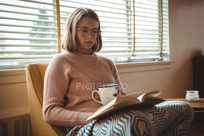 Frau liest Buch, während sie zu Hause Kaffee trinkt — Stockfoto