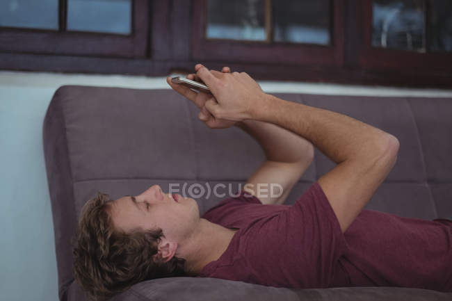 Чоловік лежить на дивані і використовує мобільний телефон у вітальні — стокове фото