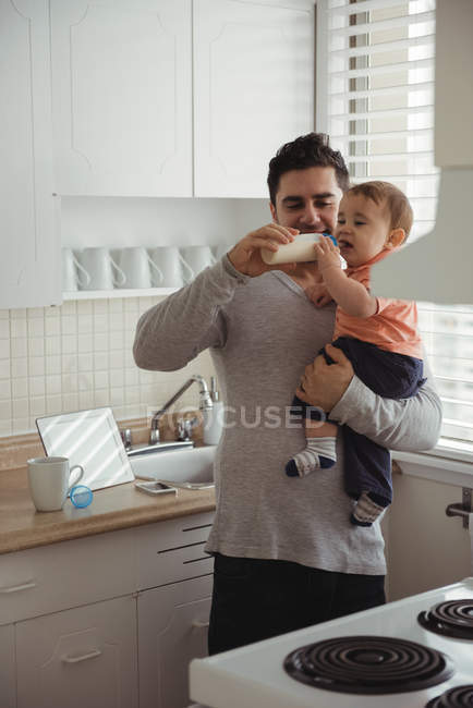 Pai alimentando menino com mamadeira de leite na cozinha — Fotografia de Stock