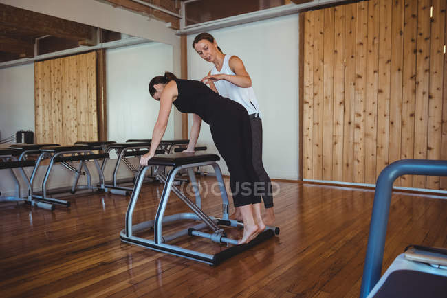 Entraîneur féminin aidant la femme tout en pratiquant pilates dans le studio de fitness — Photo de stock