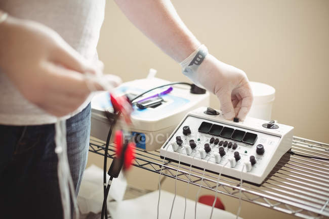 Mid section of physiotherapist adjusting electro dry needling unit in clinic — Stock Photo