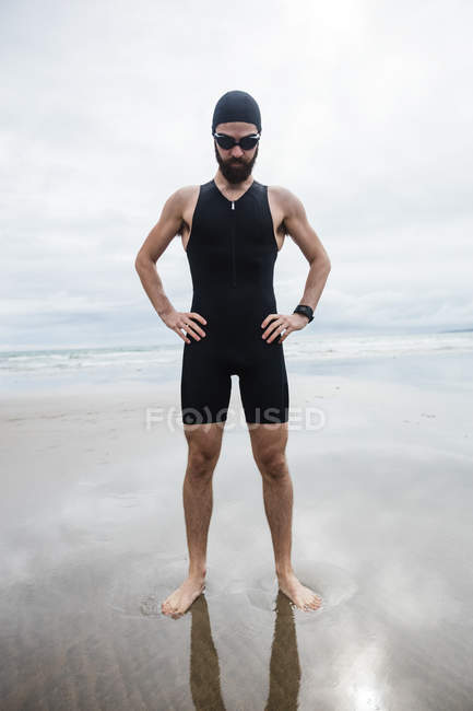 Athlete in swimming goggles standing with hand on hip at beach — Stock Photo