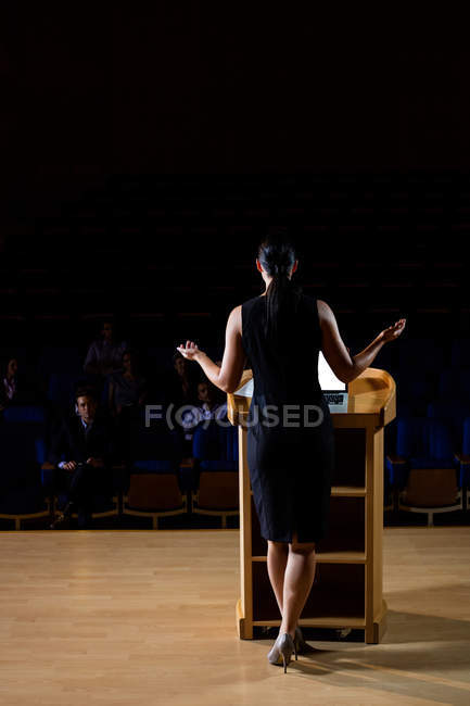 Vista trasera del ejecutivo femenino de negocios dando un discurso en el centro de conferencias - foto de stock