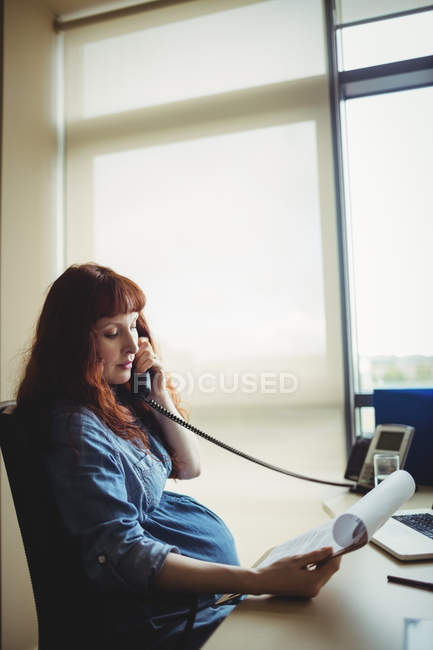 Вагітна бізнес-леді розмовляє по телефону під час роботи в офісі — стокове фото