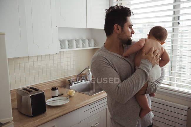 Padre reconfortante bebé mientras está de pie en la cocina - foto de stock