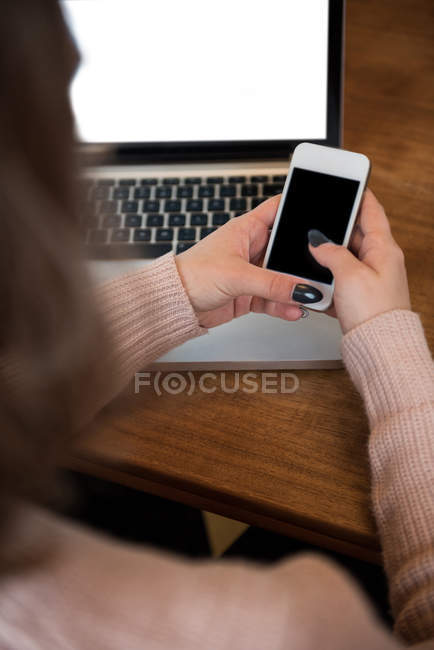 Жінка використовує мобільний телефон під час роботи на ноутбуці вдома — стокове фото