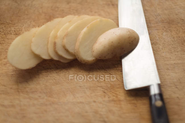 Gros plan des pommes de terre tranchées et du couteau sur la planche à découper — Photo de stock