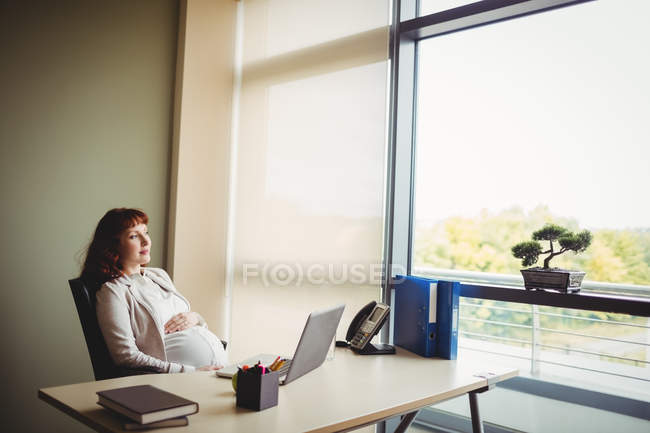 Вагітна бізнес-леді торкається живота в офісі — стокове фото