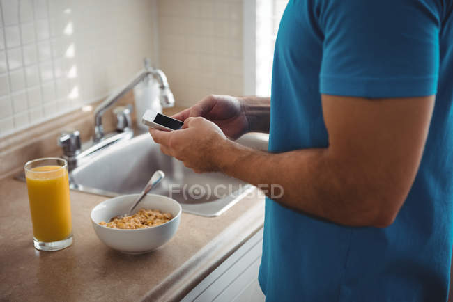 Средняя часть человека, использующего свой мобильный телефон на кухне дома — стоковое фото