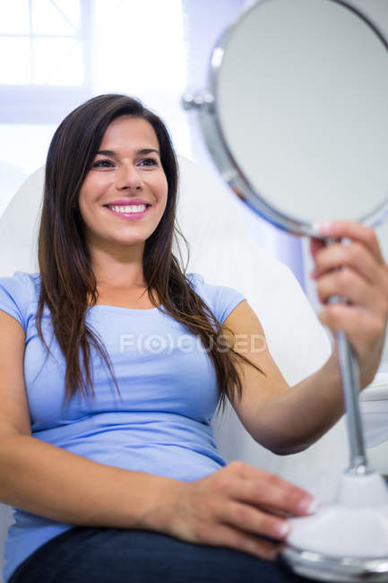 Улыбающаяся пациентка смотрит в зеркало в клинику — стоковое фото