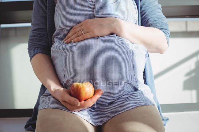Sezione centrale della donna incinta che tiene una mela a casa — Foto stock