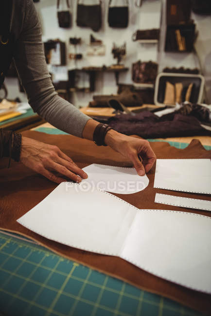Sección media de la artesana que organiza la pieza de cuero en el banco de trabajo en el taller - foto de stock