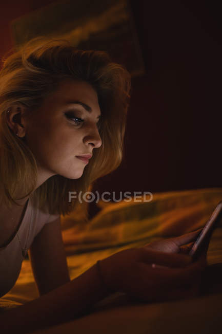 Donna sdraiata e utilizzando tablet digitale sul letto in camera da letto — Foto stock