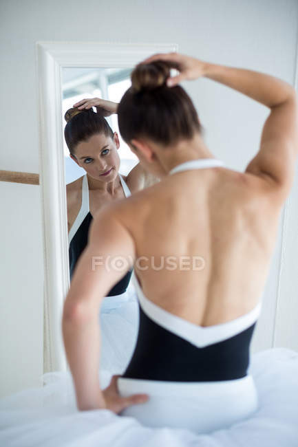 Балерина проверяет волосы перед зеркалом в балетной студии — стоковое фото