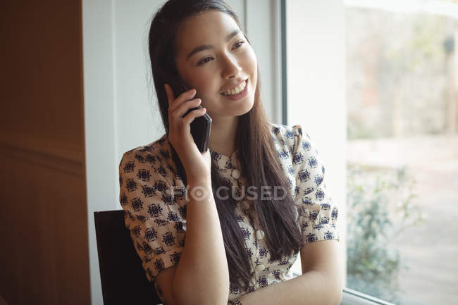 Woman talking on mobile phone near window at cafe — Stock Photo