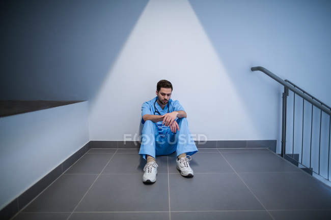 Напряженная медсестра сидит в коридоре больницы — стоковое фото