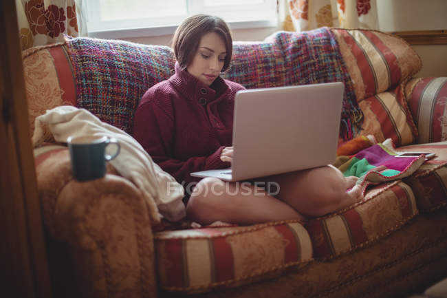 Schöne Frau sitzt auf dem Sofa und benutzt Laptop im Wohnzimmer zu Hause — Stockfoto