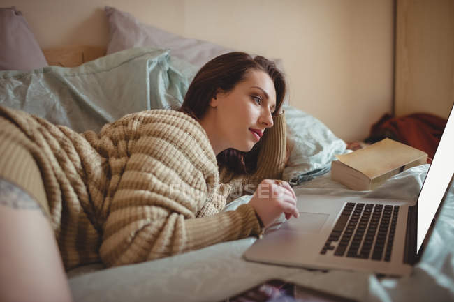 Belle femme couchée et utilisant un ordinateur portable sur le lit à la maison — Photo de stock