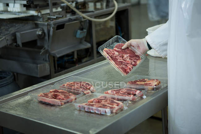 Mani di macellaio organizzare bistecche in vassoio in fabbrica di carne — Foto stock