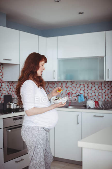 Mulher grávida tendo salada na cozinha em casa — Fotografia de Stock