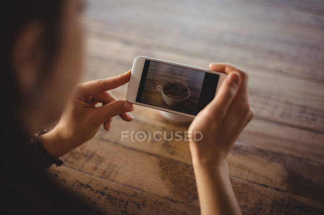 Woman clicking photo of coffee cup in cafe — Stock Photo