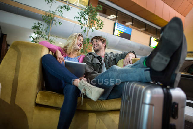 Pareja sonriente interactuando entre sí en la zona de espera en la terminal del aeropuerto - foto de stock