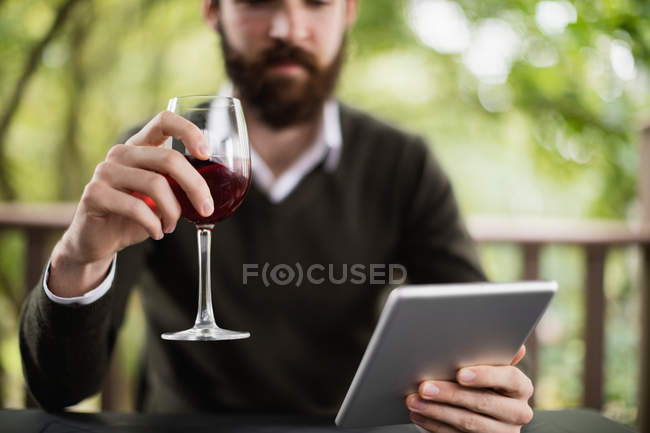 Homem usando tablet digital enquanto toma um copo de vinho no bar — Fotografia de Stock