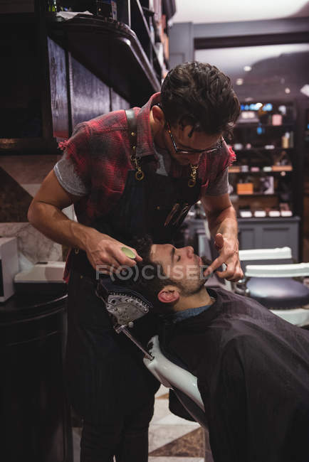 Barbiere applicando crema su barba di cliente in negozio di barbiere — Foto stock