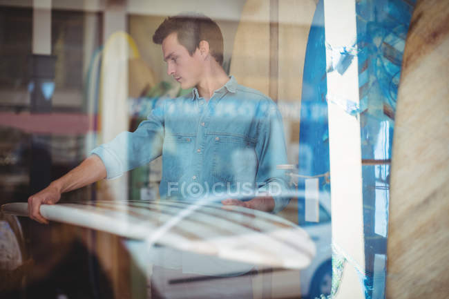Hombre seleccionando tabla de surf en una tienda detrás de la ventana - foto de stock