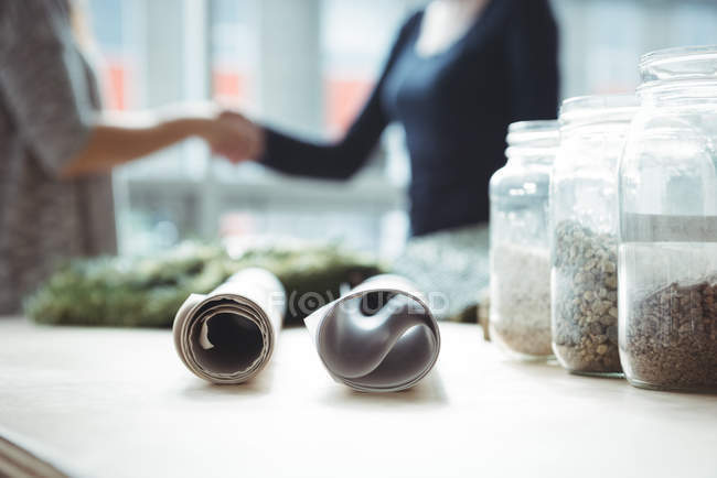 Sample of pebbles in jar and blueprint on table at office — Stock Photo