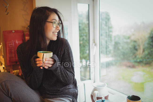 Donna sorridente che tiene una tazza di caffè in cucina a casa — Foto stock