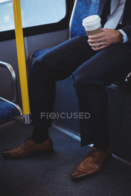 Section basse de l'homme d'affaires tenant une tasse de café jetable tout en voyageant dans le bus — Photo de stock
