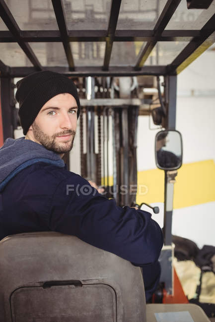Retrato del mecánico sentado en la carretilla elevadora en el garaje de reparación - foto de stock