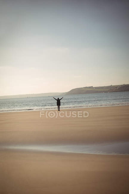 Задний вид женщины, стоящей с протянутыми руками на пляже днем — стоковое фото