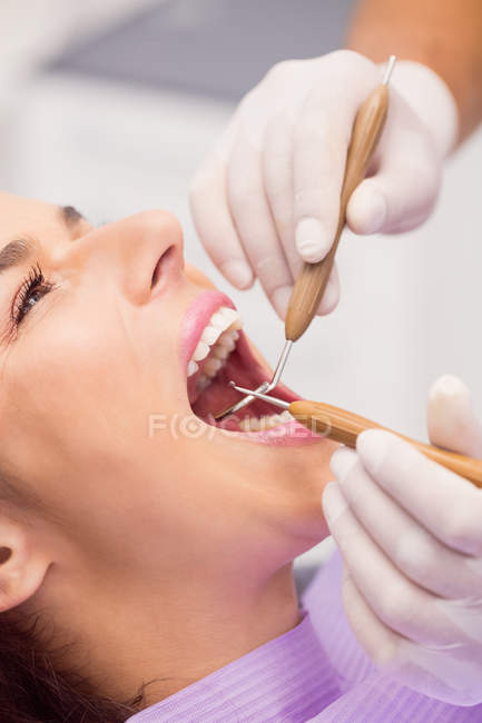 Крупный план стоматолога, осматривающего женские зубы с помощью инструментов — стоковое фото