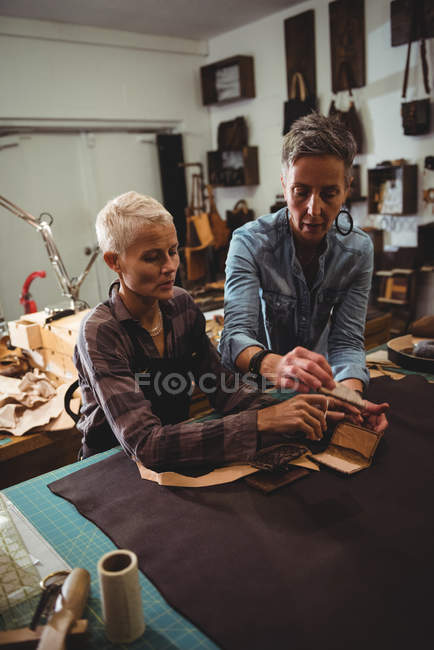 Craftswomen discussing over a sheet of leather in workshop — Stock Photo
