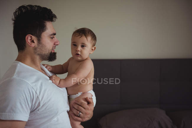 Мужчина держит своего ребенка, стоя в гостиной дома — стоковое фото