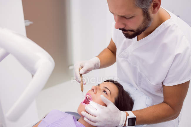 Стоматолог вивчає жіночі зуби пацієнта з дзеркалом рота в клініці — стокове фото