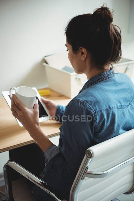 Business executive using digital tablet while having cup of coffee in office — Stock Photo