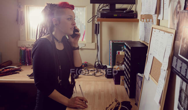 Cabeleireiro feminino falando no telefone celular na loja dreadlocks — Fotografia de Stock