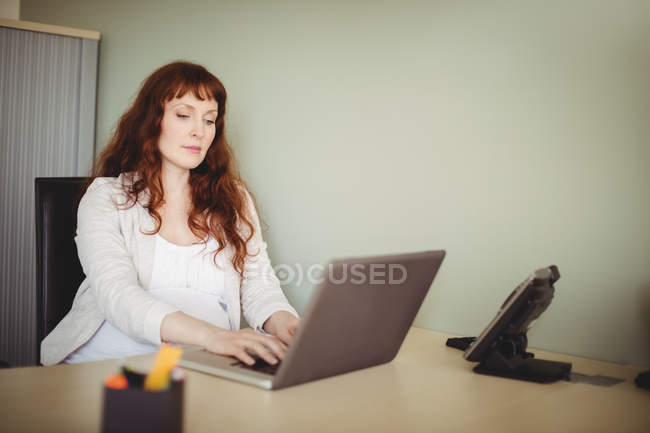 Вагітна ділова жінка використовує ноутбук в офісі — стокове фото