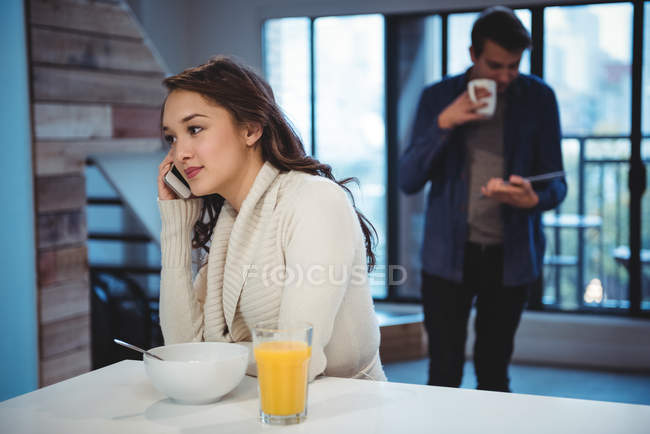 Mulher falando no celular enquanto toma café da manhã em casa — Fotografia de Stock