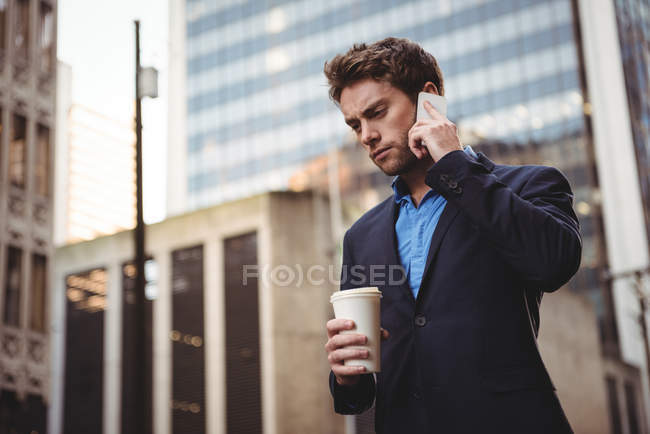 Бізнесмен розмовляє по мобільному телефону і тримає каву на вулиці — стокове фото