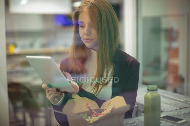 Woman using digital tablet while eating salad in the restaurant — Stock Photo