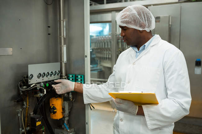 Male worker holding clipboard while operating machine in juice factory — Stock Photo