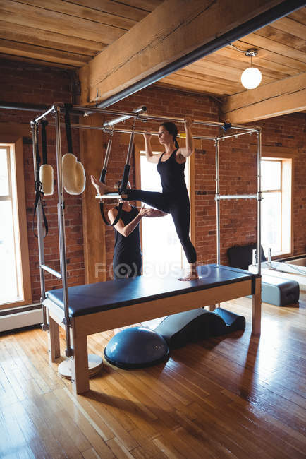 Instructor ayudando a la mujer mientras practica pilates en el gimnasio - foto de stock